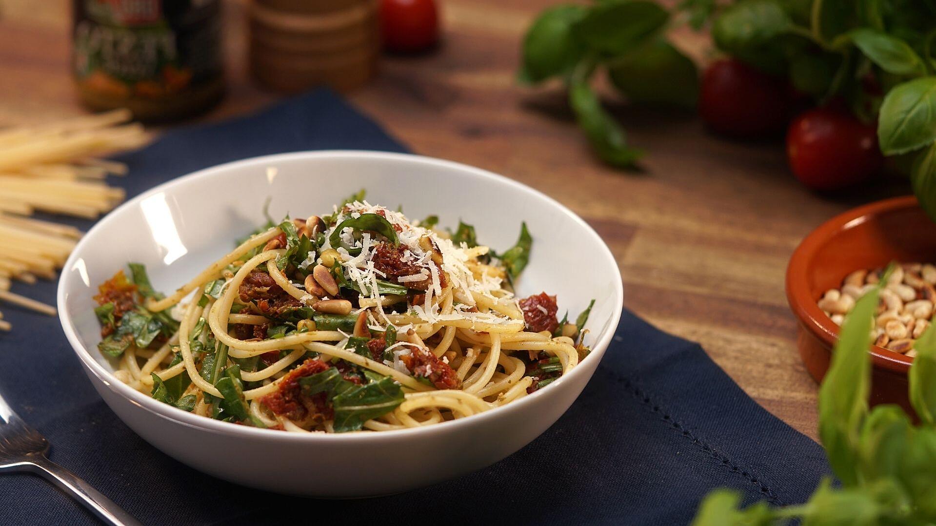 Eine Schüssel mit italienischem Spaghettisalat bestehend aus Rucola, getrockneten Tomaten, Spaghetti und Parmesan.
