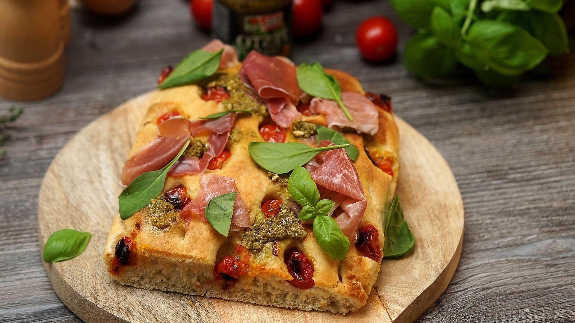 Focaccia mit grünem Pesto und Parma Schinken liegt auf einem Holzbrett