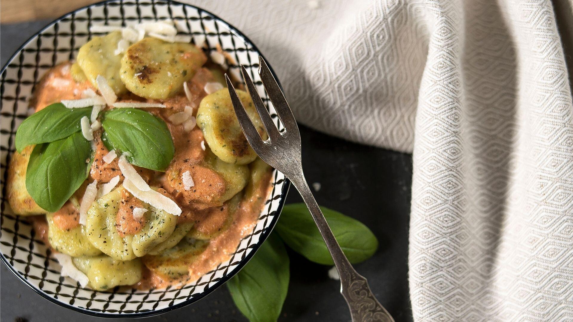 Basilikum-Gnocchi angerichtet auf einem weißen Teller mit schwarzem Karo-Muster, daneben eine graue Serviette
