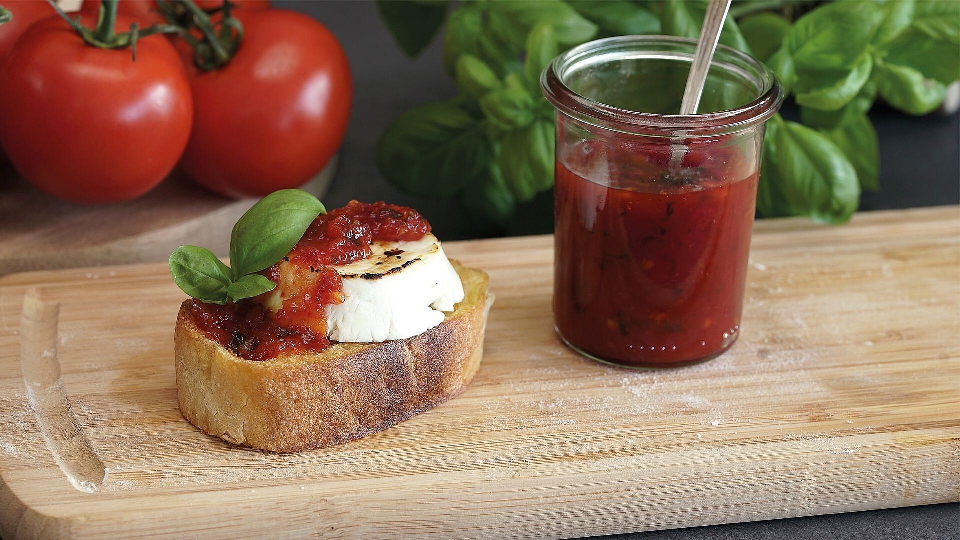 Auf einem Holzbrett liegt eine Scheibe Ciabatta mit gratiniertem Ziegenkäse und Tomatenmarmelade