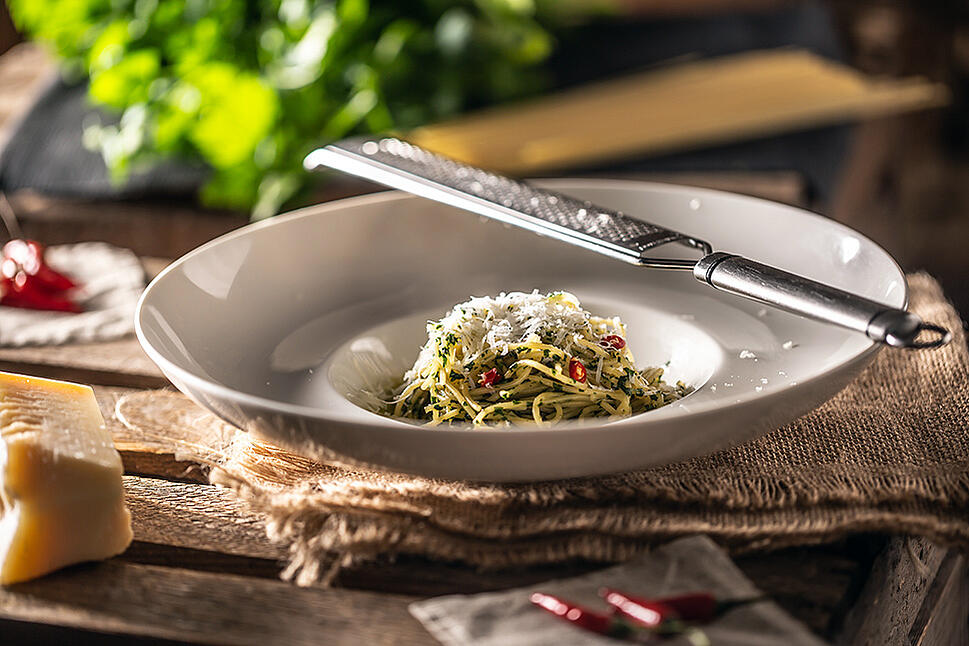 A plate contains spaghetti with Parmesan, oil, and chili. A Parmesan grater is placed on top of it.
