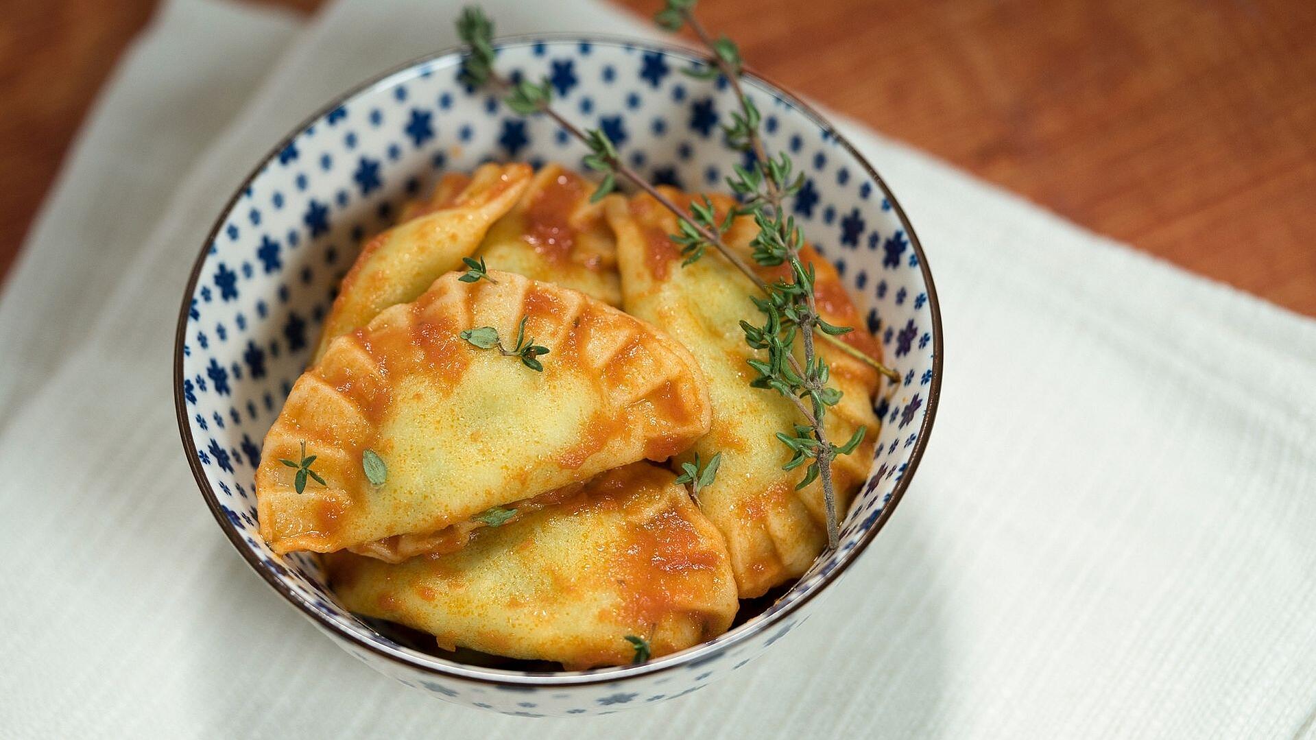 Ravioli mit Tomatensauce in einer Schüssel angerichtet und mit Kräutern garniert