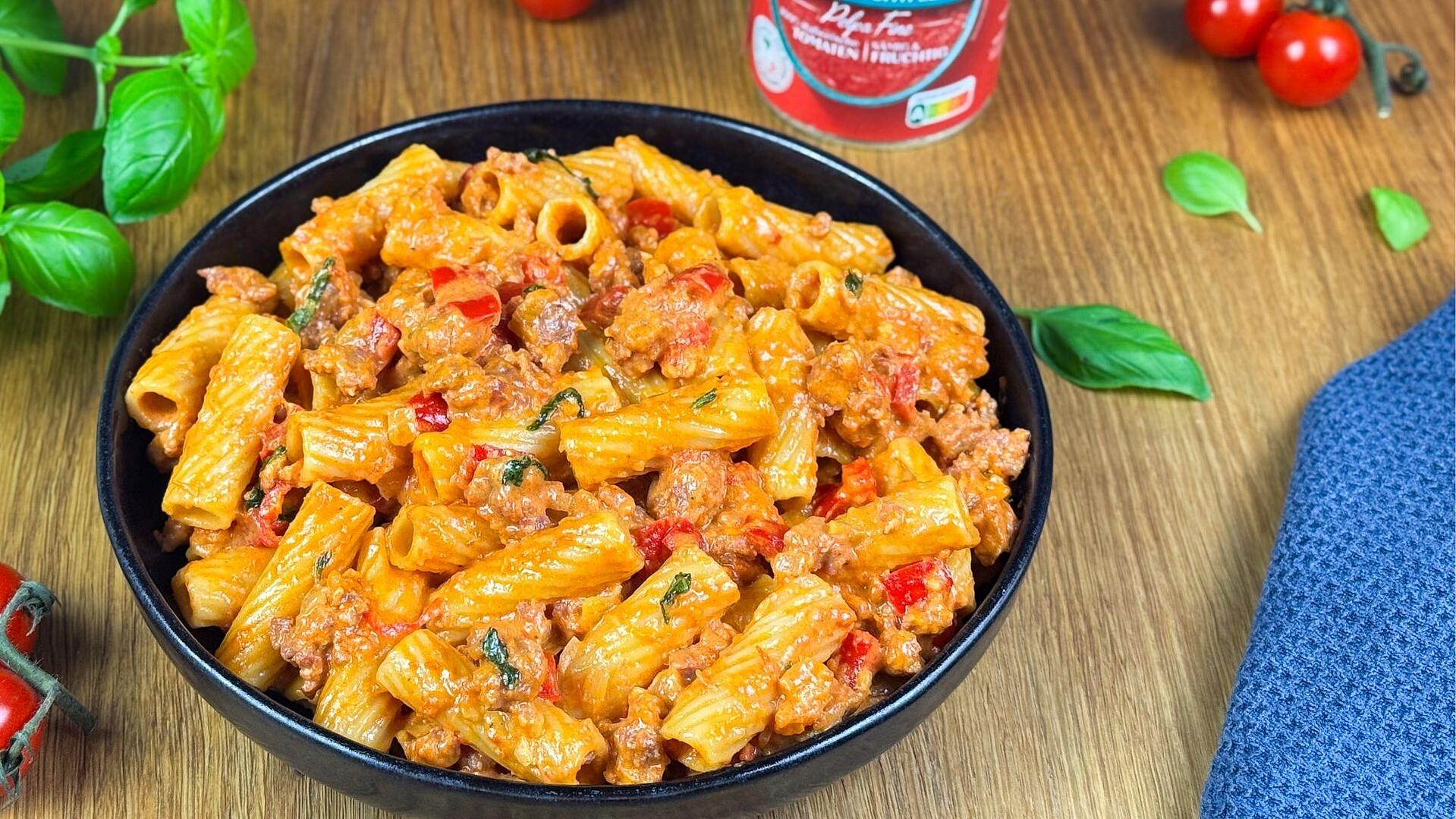 Ein Teller gefüllt mit cremiger Salsiccia Pasta und umgeben von frischem Basilikum und Tomaten 