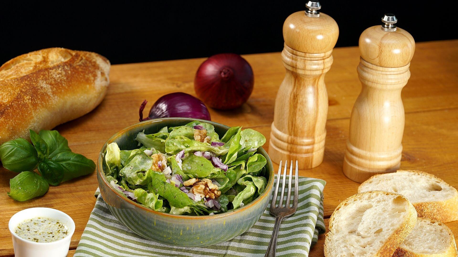 Eine Schüssel mit grünem Salat, Zwiebeln, Walnüssen und Dressing