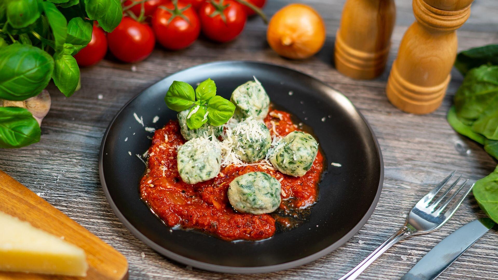 Gnudi in Tomatensauce auf einem schwarzen Teller, mit Basilikum garniert