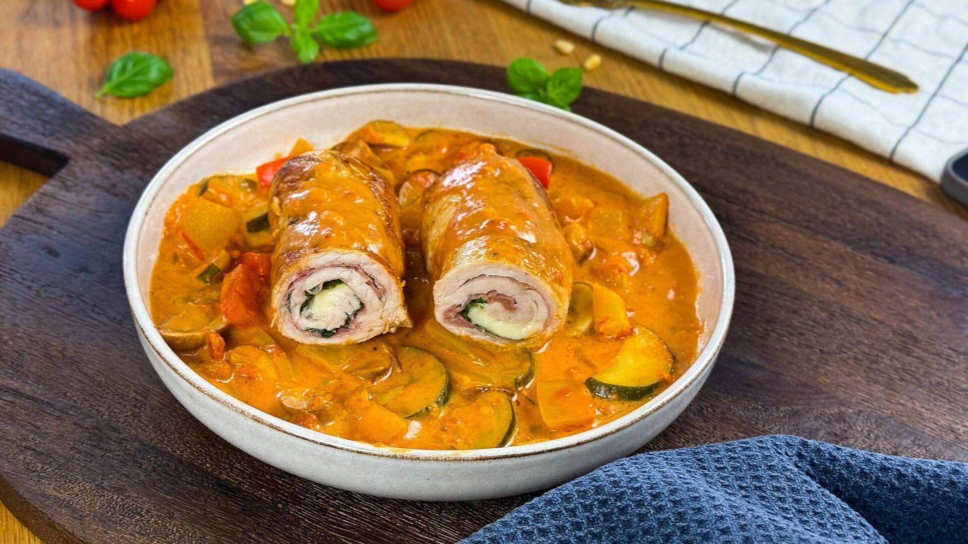 Puten-Involtini mit mediterranem Pfannengemüse in cremiger Soffritto-Sahnesoße – angerichtet im Topf auf einem rustikalem Holzbrett.