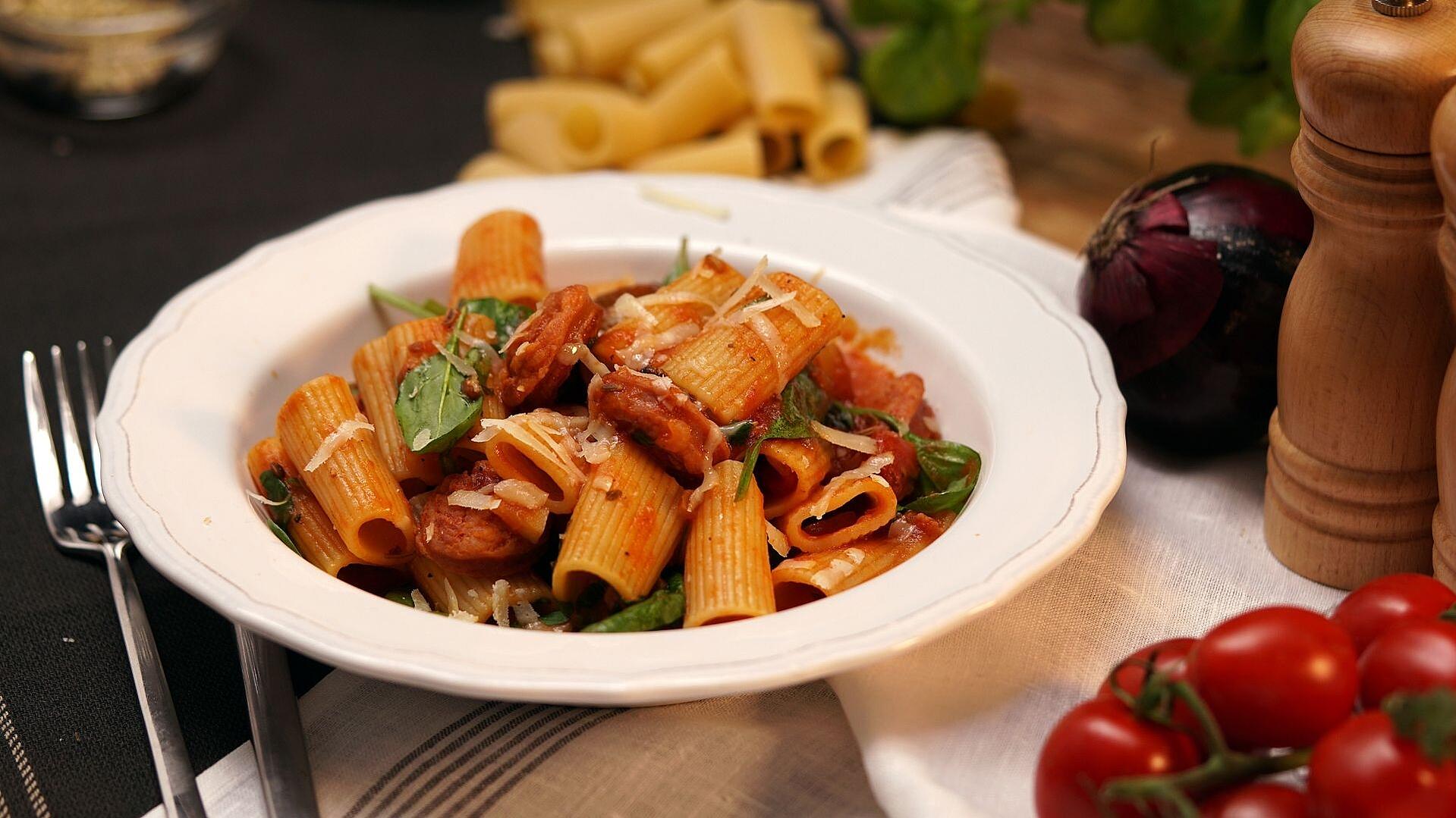 Rigatoni-Nudeln mit Salsiccia-Tomatensauce auf einem weißen Pastateller