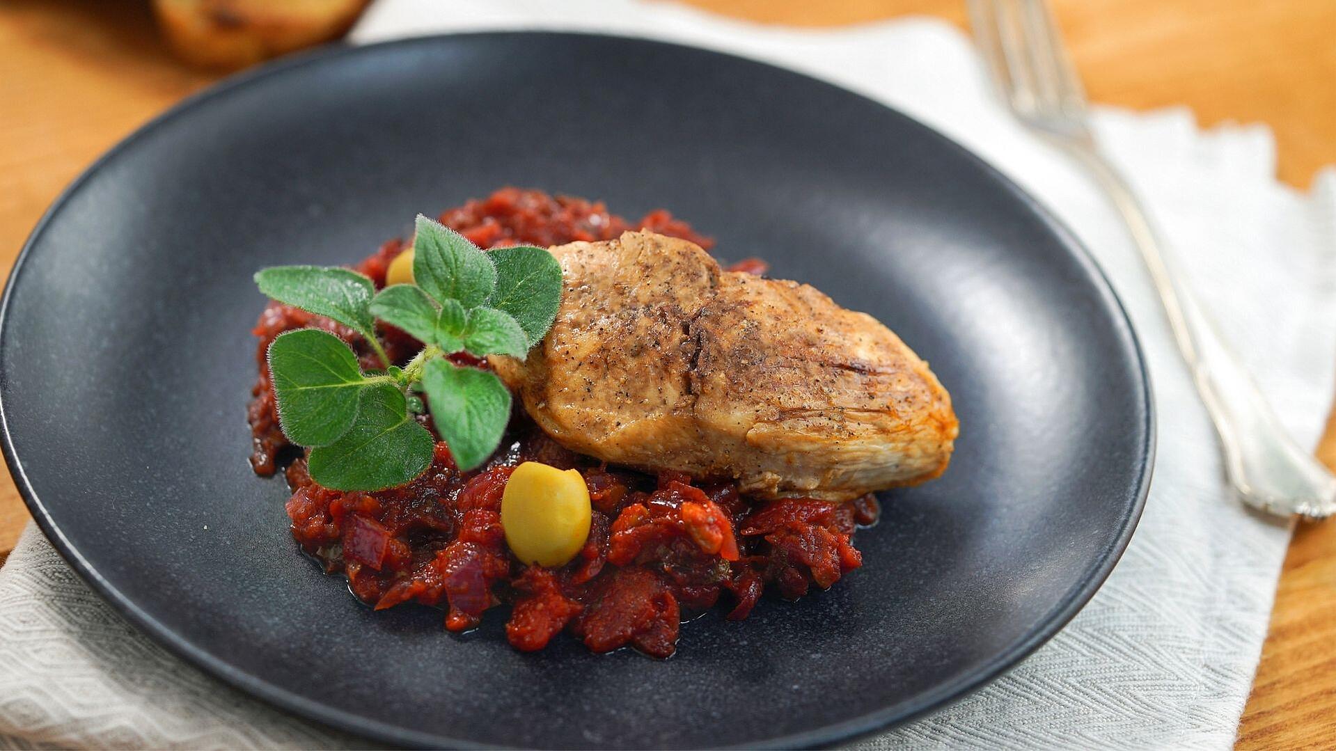 Ein schwarzer Teller mit Hähnchenbrust auf Tomaten-Oliven-Sauce 