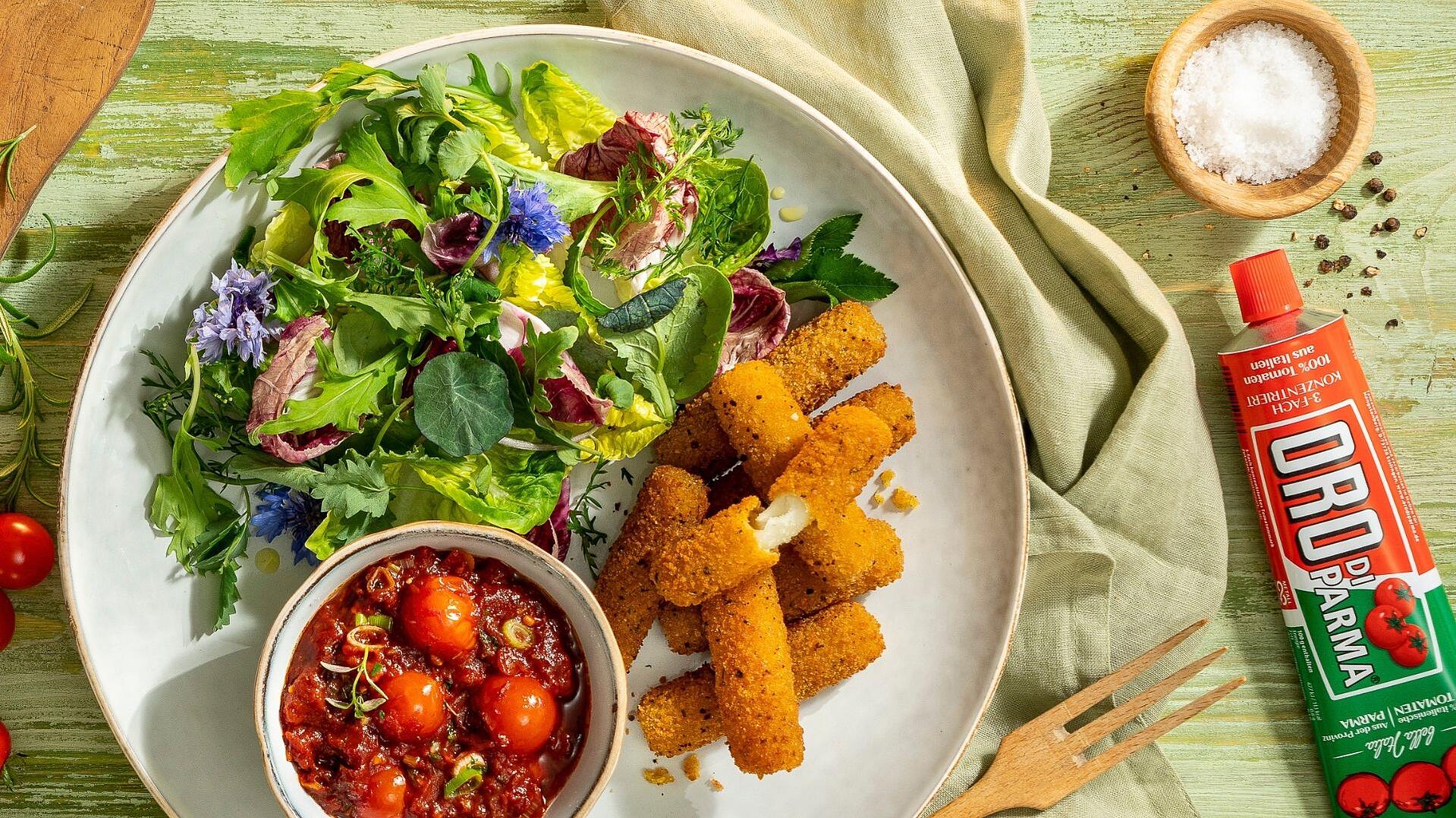 Selbstgemachte Mozzarella-Sticks in einer Schüssel, daneben eine kleinere Schüssel mit Kirschtomaten-Kräuter-Dip
